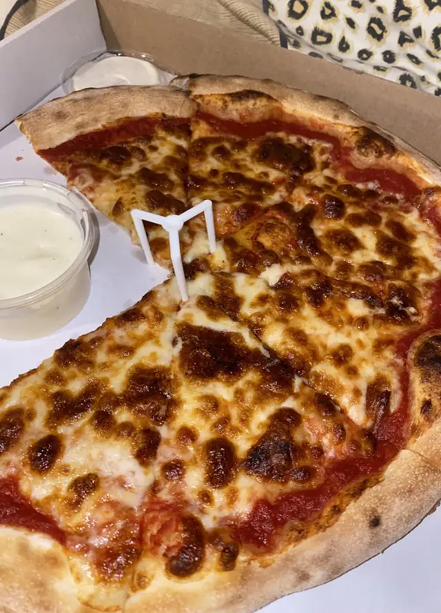 Złocista pizza z bąblami sera prosto z pieca, w kartonie z sosem czosnkowym